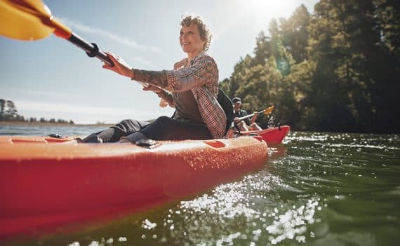 Middle - aged, heart - healthy woman paddling a red canoe on a sunny day