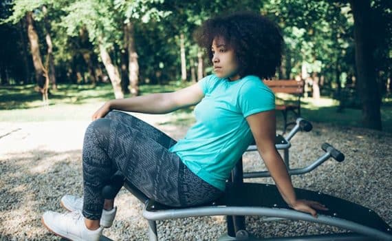 Young African - American woman sitting on sit - up bench in park