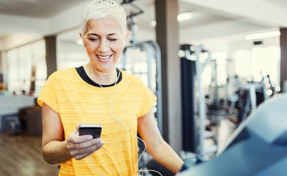 Mature Woman Exercising on treadmill in the gym and using smartphone fitness app.