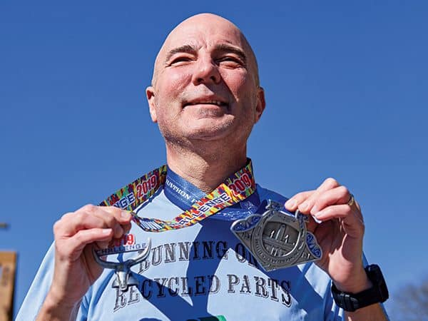 Transplant patient Mike Barker wears Cowtown Half Marathon medals and shirt that says “running on recycled parts.”