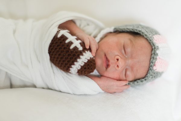 Baby in the NICU wears a crochet football helmet.