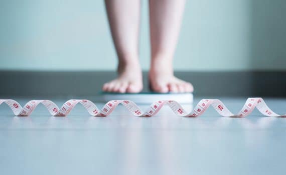 Feet standing on scale with measuring tape in foreground; person is considering weight-loss surgery.