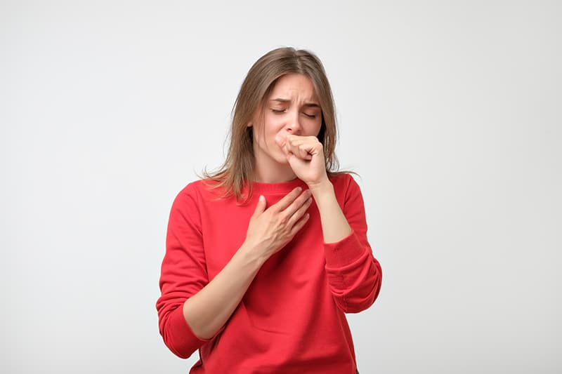 Woman holding chest and coughing; learn about cough care.
