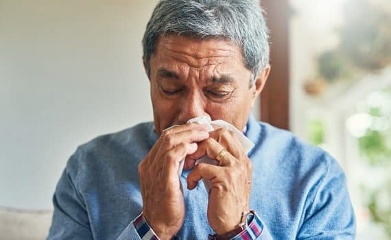 Older adult blowing his nose; flu vaccines can help lessen the risk of getting the flu.