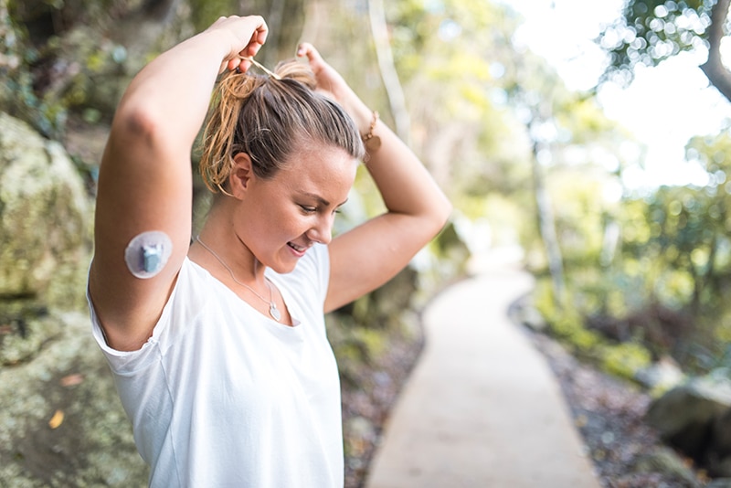 Woman outside in T-shirt with an insulin patch for managing diabetes on her arm.