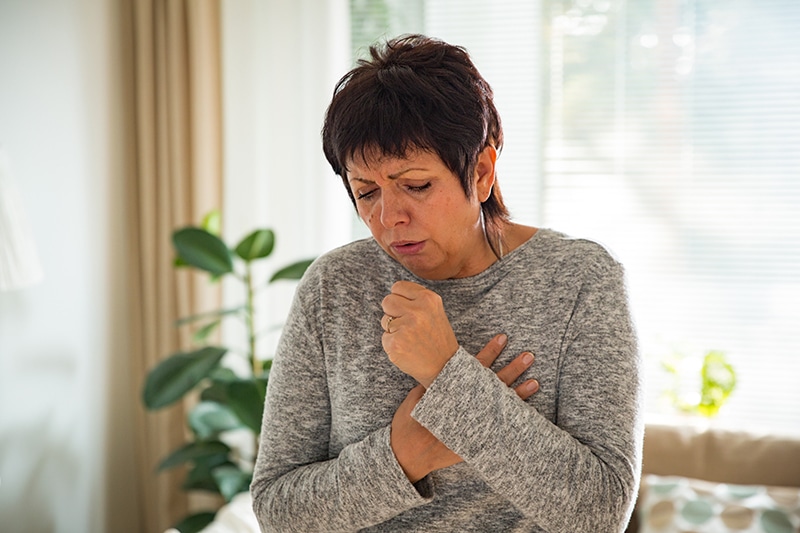 Woman coughs, showing possible symptoms of COVID-19, flu or cold.