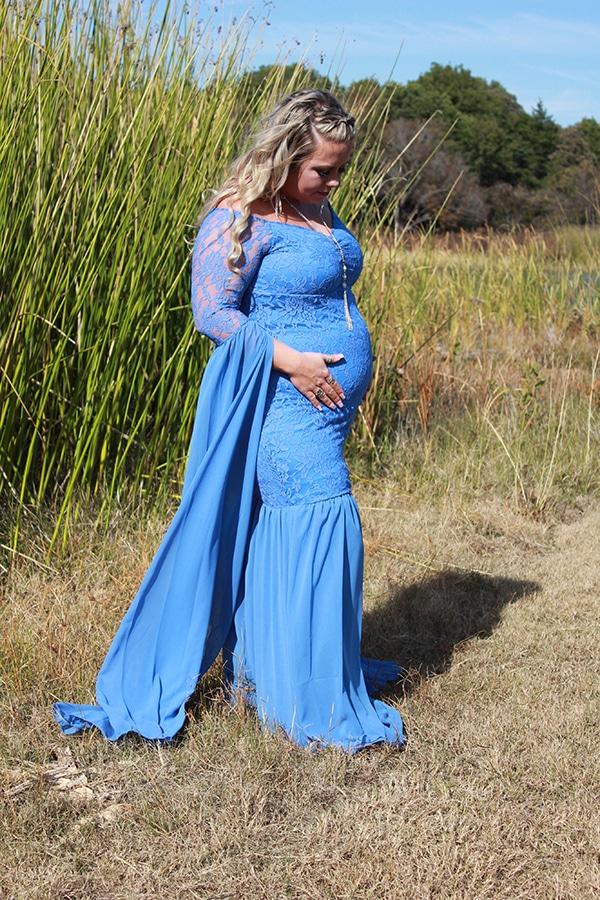 Whitney Monroe, weight-loss surgery patient, stands in field in blue lace dress, holding her baby bump and looking down.