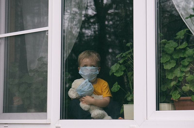 child looking out of window wearing face mask to protect against COVID-19
