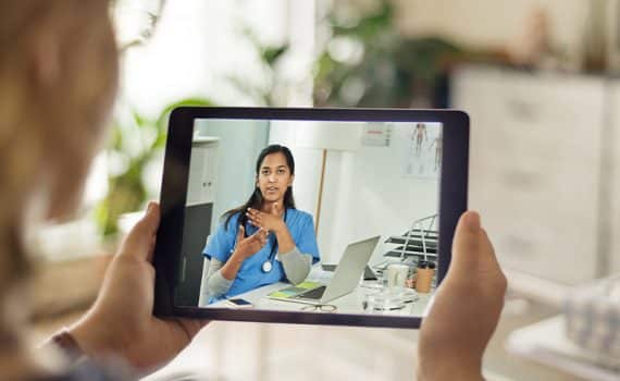 patient uses telemedicine to meet with a doctor in scrubs on tablet