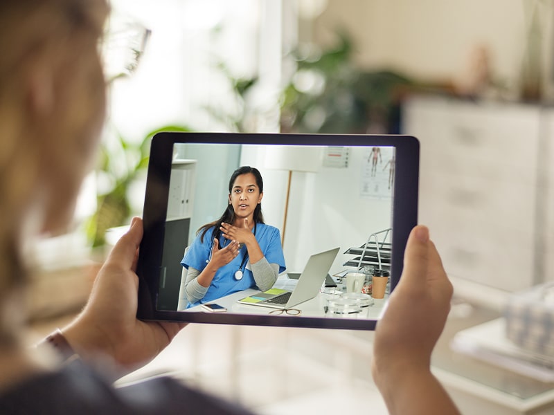 patient uses telemedicine to meet with a doctor in scrubs on tablet