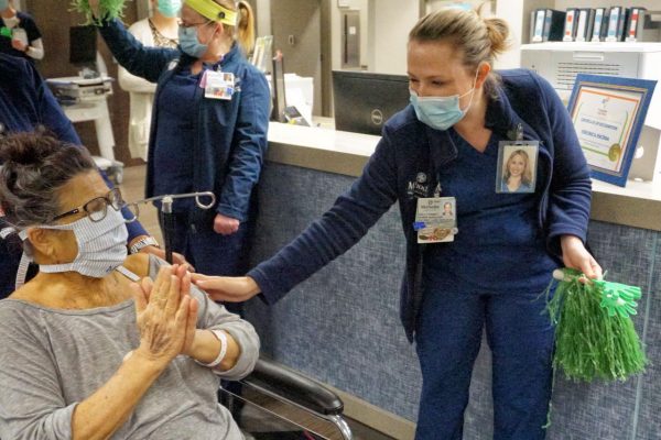 Barbara Winn exiting the hospital on wheelchair while nurses clap, wave, and congratulate her