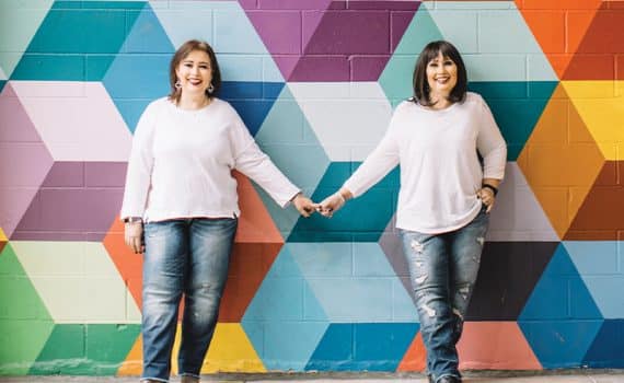 Twin sisters Yvette and Yvonne, standing in front of colorful rainbow wall mural after Yvette's victory over breast cancer with the help of Methodist Charlton Medical Center