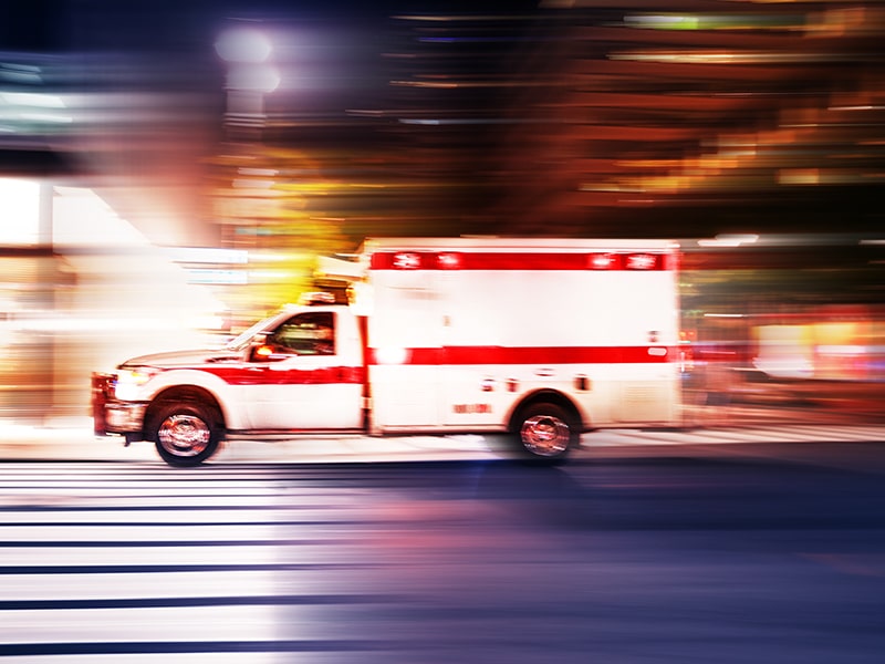 ambulance driving quickly through a street at night, used to explain COVID-19 fears