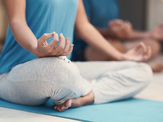 Woman in gray leggings and a blue tank top sitting criss-cross on the floor on a bright blue yoga mat