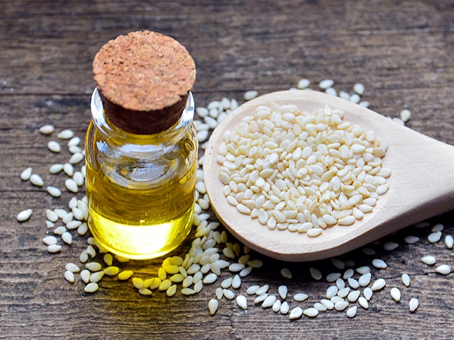 Small jar of oil with cork on the top with sesame seeds on a wooden spoon