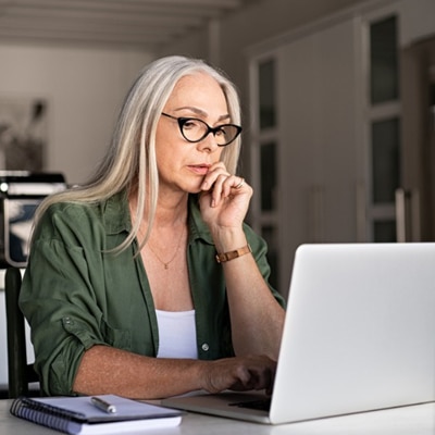 Woman with black glasses looks at laptop with her left hand on her face