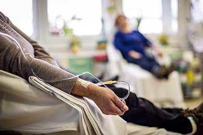 Photo of two people sitting in a medical facility receiving medication through an IV