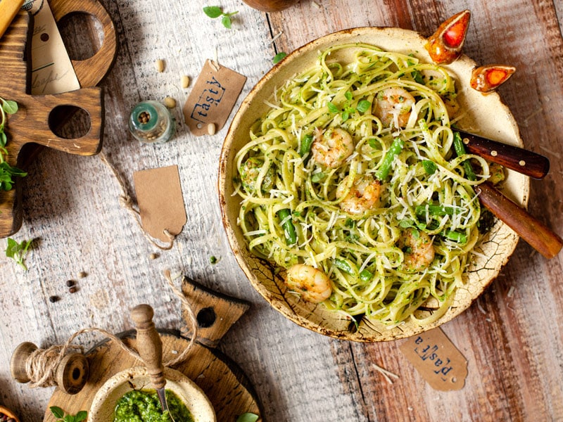 Italian food dish with shrimp and pesto with spaghetti in a wooden bowl, resting on a tablecloth and wooden table