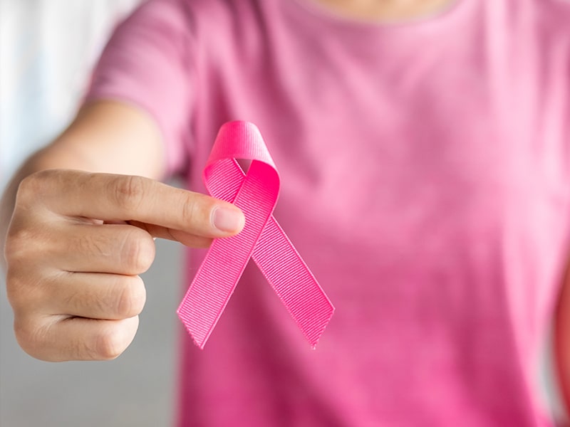 Person wearing pink shirt and holding pink breast cancer awareness ribbon in front of the camera