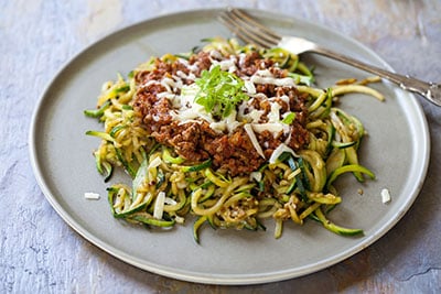 Pasta dish with spaghetti, zucchini noodles, sauce, cheese, and green garnish