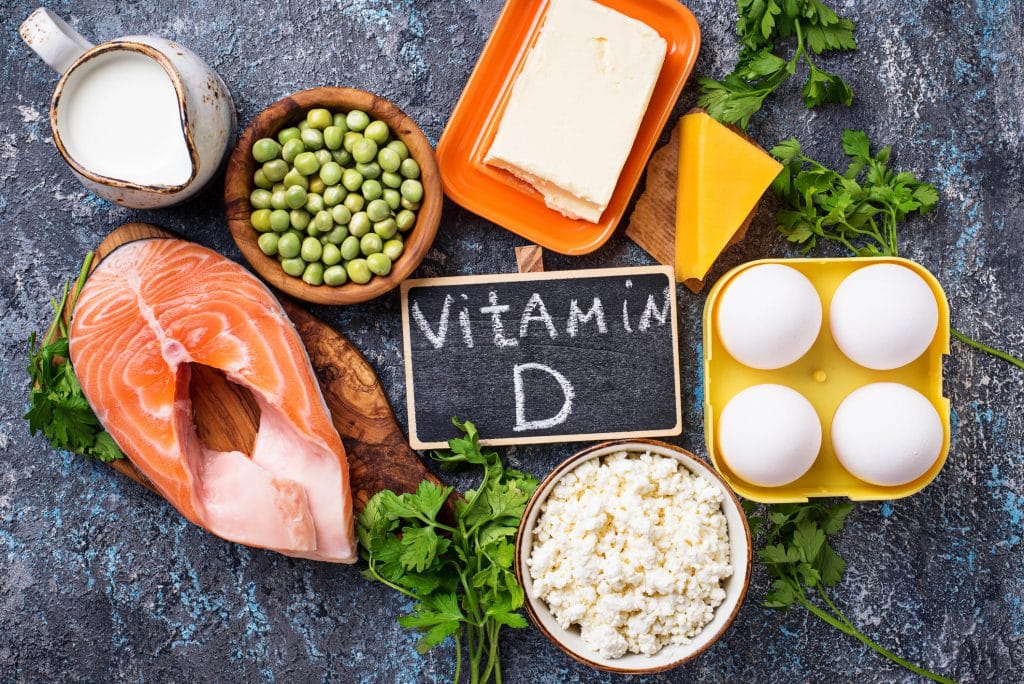 Chalkboard with "Vitamin D" written on it, surrounded by foods such as salmon, rice, cheese, peas, and more.