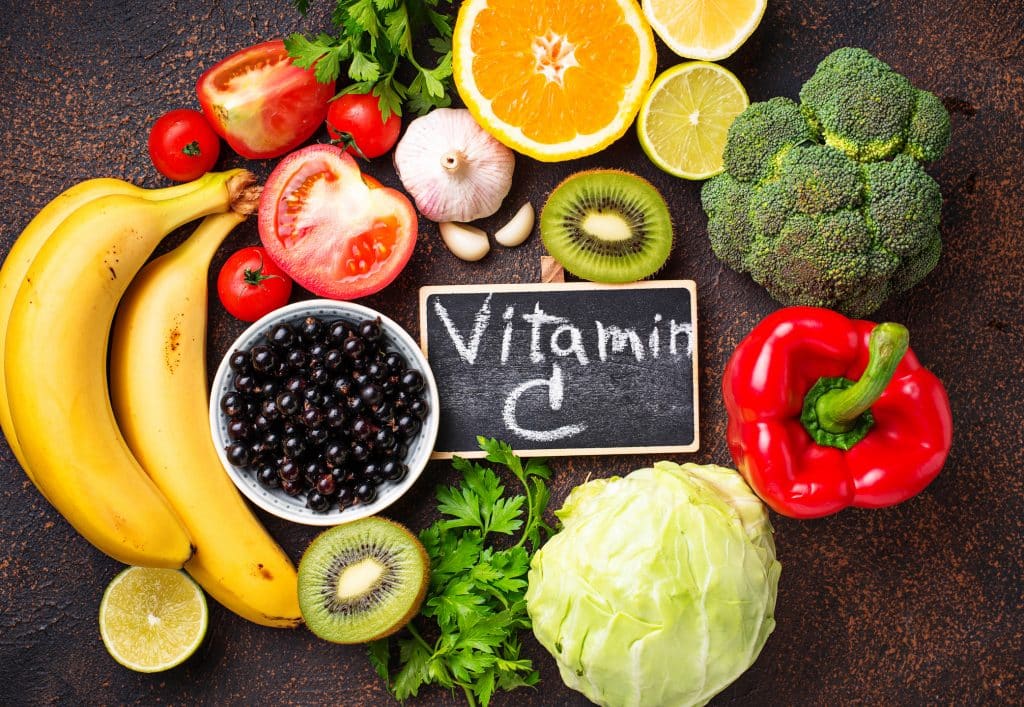 Chalkboard with "Vitamin C" written on it, surrounded by foods such as bananas, kiwis, cabbage, peppers, broccoli, oranges, garlic, and tomatoes