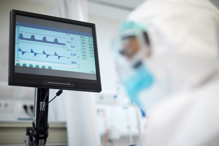 Medical professional in protective clothing and goggles looks at monitor to track vital signs