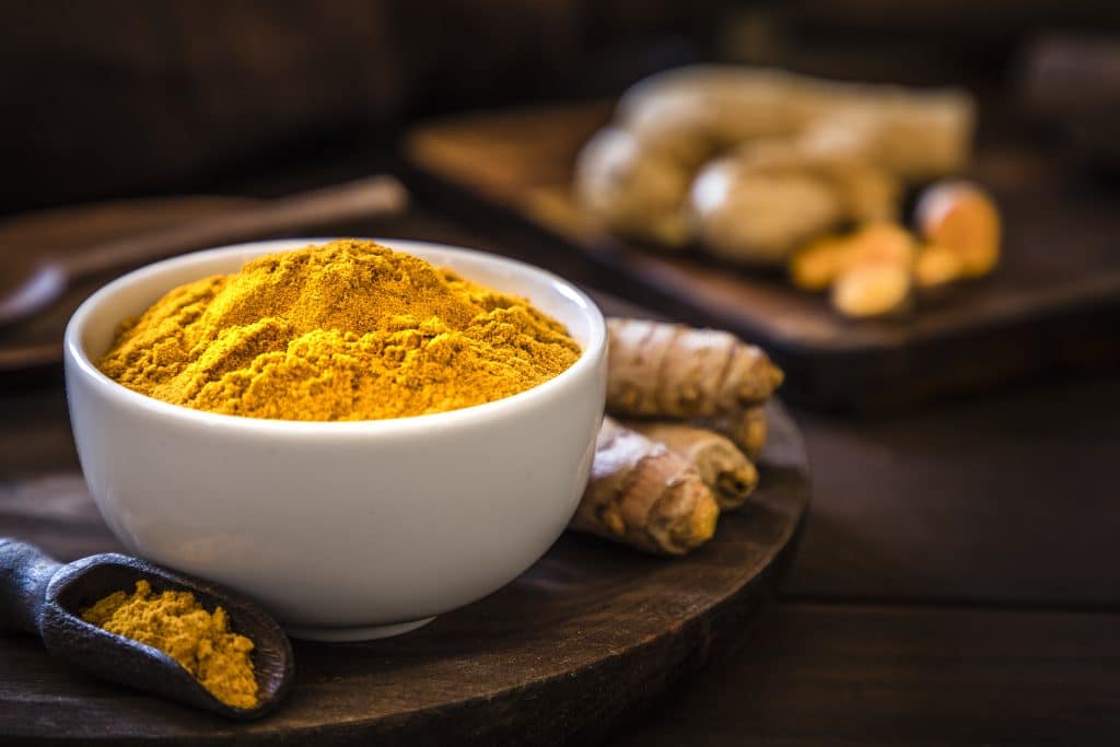 Raw and ground turmeric presented on a wood board and a white bowl