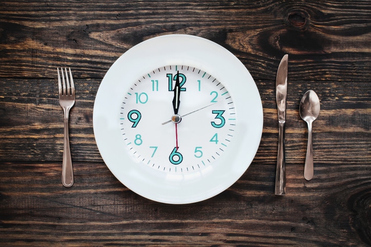 A plate with a clock on it and table setting with silverware 