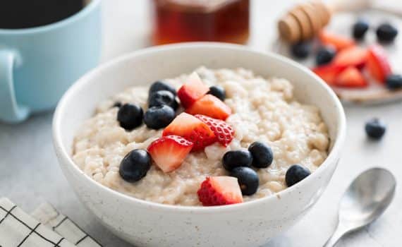 Oatmeal porridge with berries, honey and cup of coffee, at a table setting with coffee and other breakfast foods