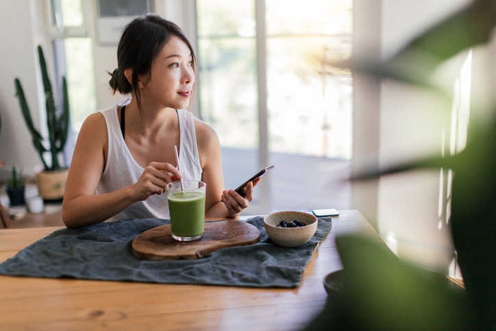 A woman enjoying a green smoothie and a bowl of breakfast food