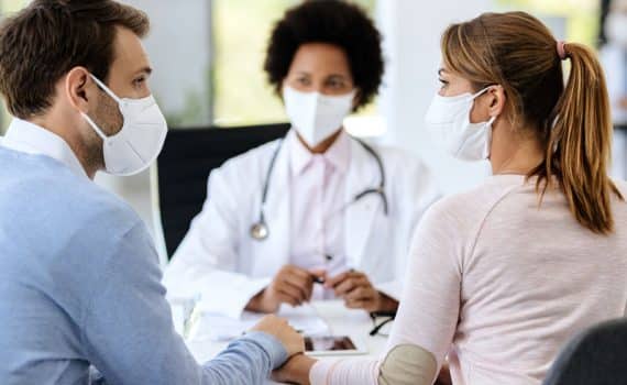 A man and a woman talking with a medical professional while wearing face masks, used to explain infertility issues