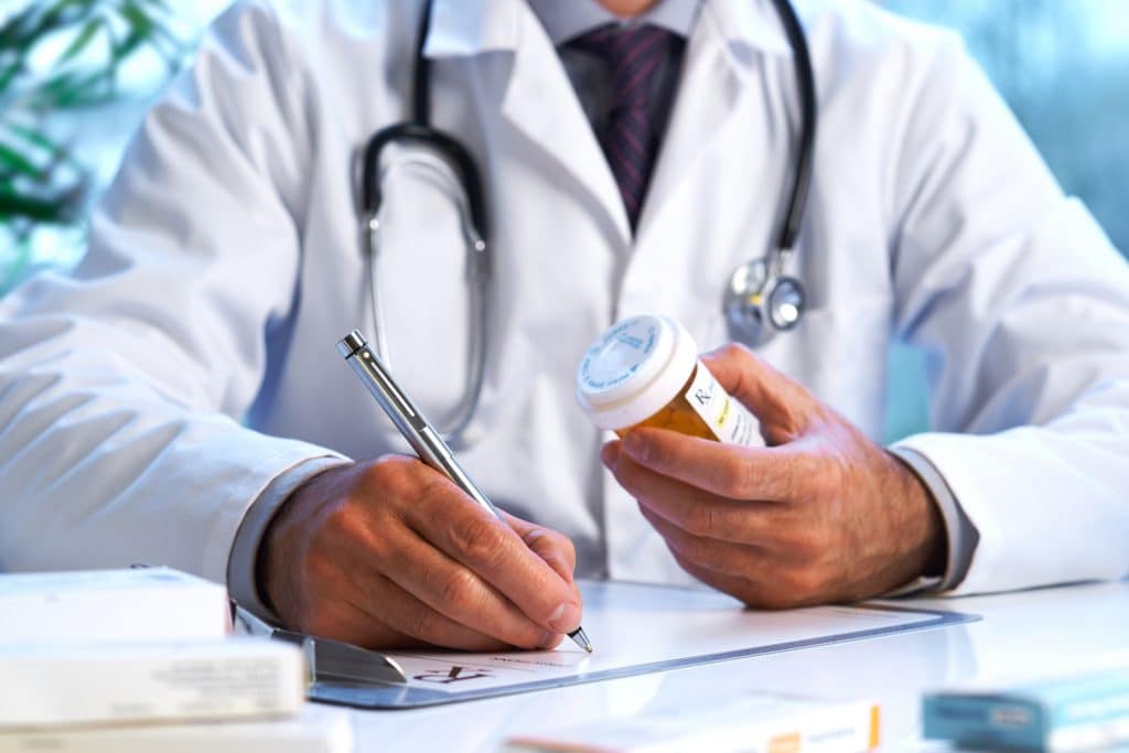 A physician writing out a prescription while holding a medicine bottle