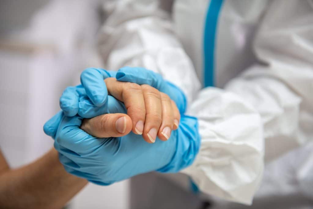 A medical professional with blue gloves and scrubs holds a hand