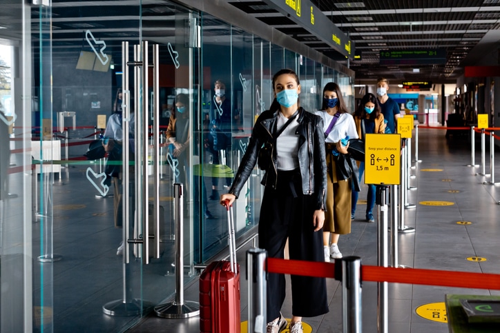 A socially distanced line of masked people holding suitcases