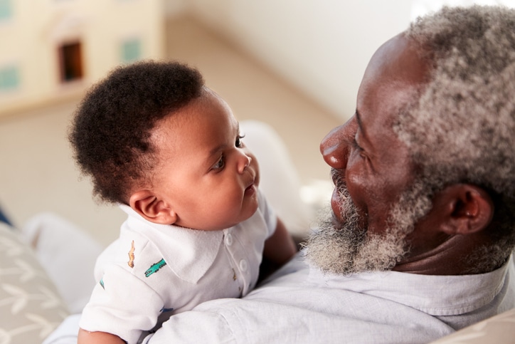 An older man hugging and embracing a young baby, used to explain safe actions after getting vaccinated for COVID-19.