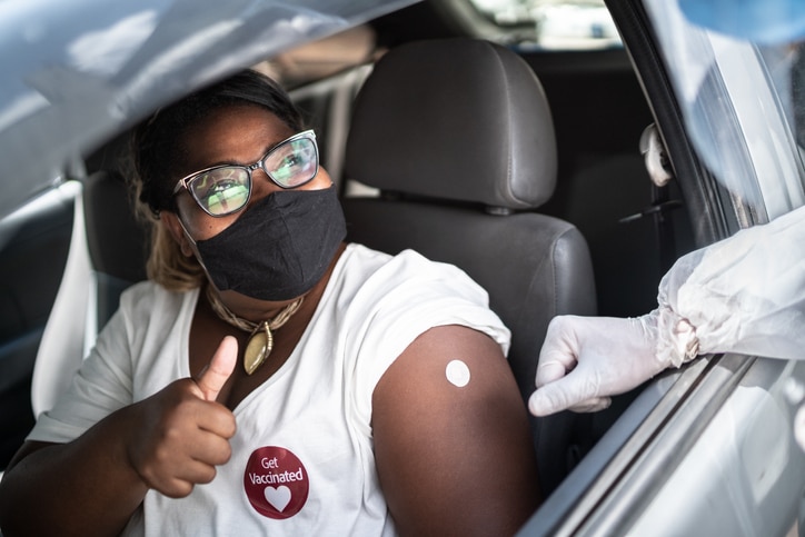 A masked woman giving a thumbs up after getting vaccinated