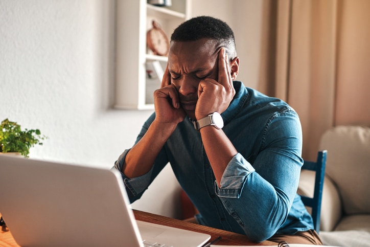 A man sitting in front of a computer, putting pressure and stress on his head with his fingers