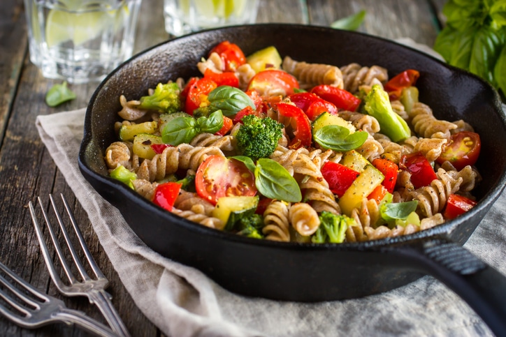 Whole wheat pasta with spinach, tomatoes, and vegetables in a cast iron pan