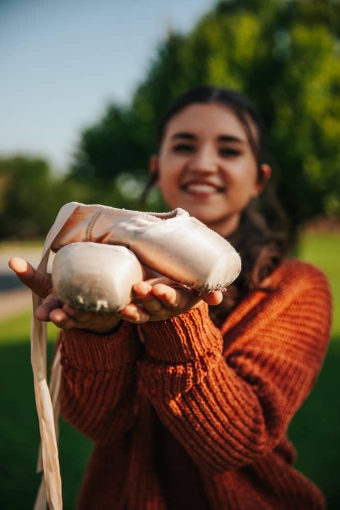 Chloe Galvez smiling at the camera and holding her ballet shoes