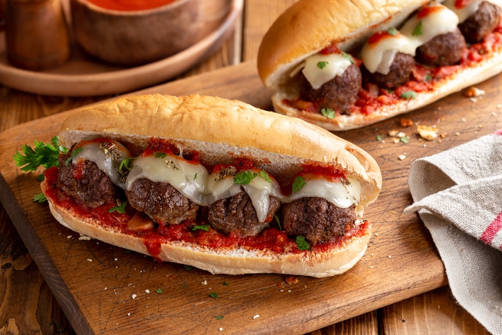 Meatball hoagies with cheese and marinara sauce on a wood cutting board