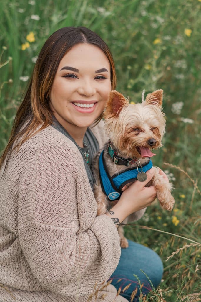 Amy Jackson photographed with her Yorkie in a field while wearing a pink cardigan, gray shirt and jeans.