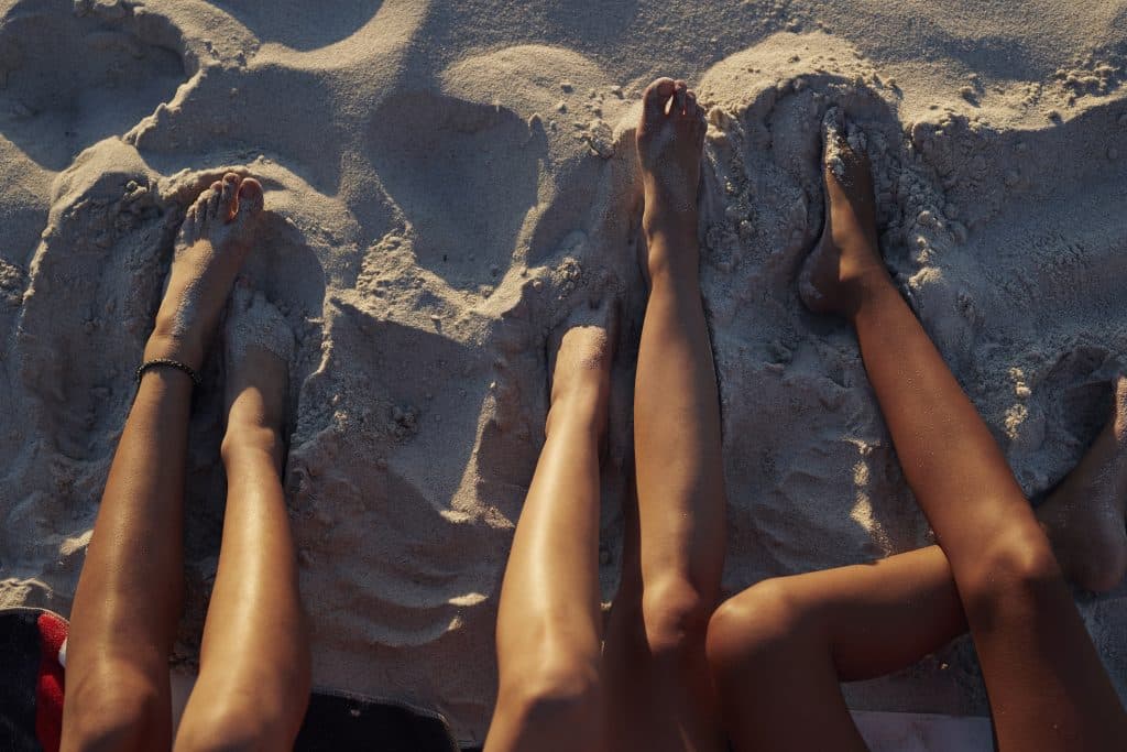 Three sets of feet and legs in the sand, used to explain summer foot care tips