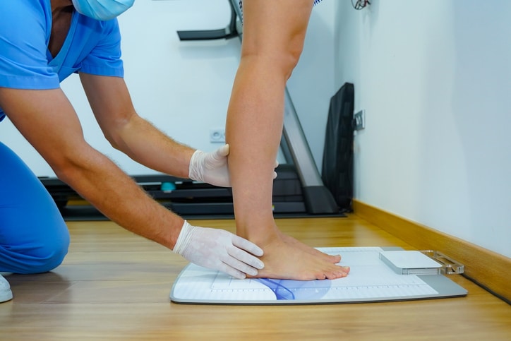 A medical professional assisting someone standing and supporting their feet