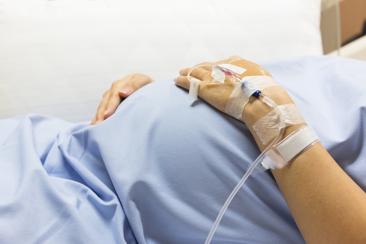 A pregnant patient in a hospital gown and with an IV in their arm