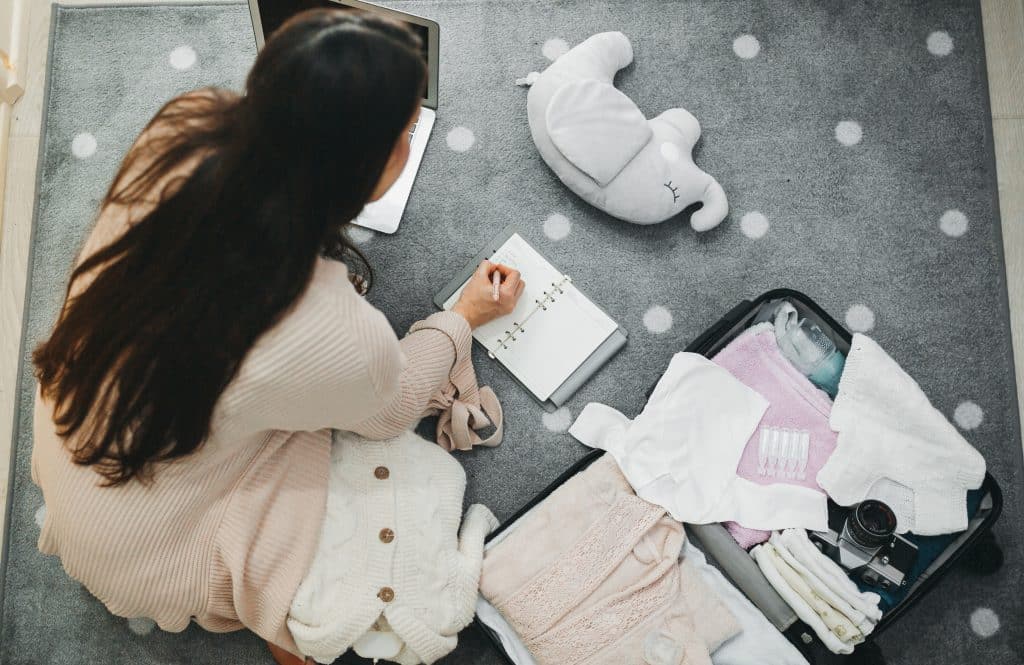 A woman surrounded by new baby clothes and toys, writing notes and a birth plan in a notebook