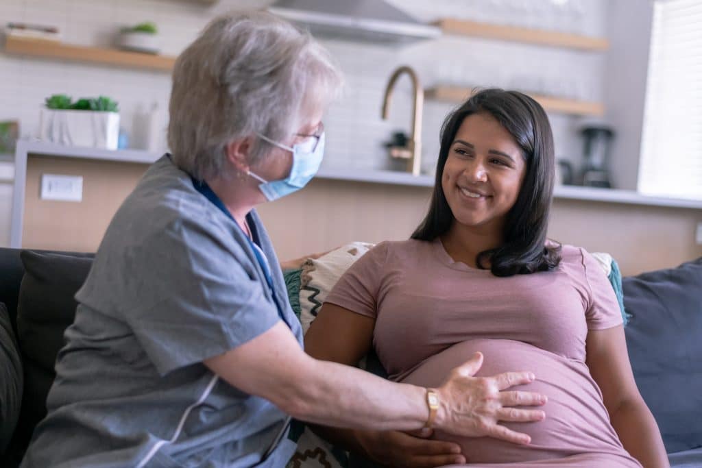 A pregnant woman smiling at a person wearing a mask