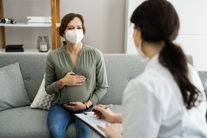 A pregnant woman holding her belly and speaking to a medical professional, possibly about a birth plan or labor details