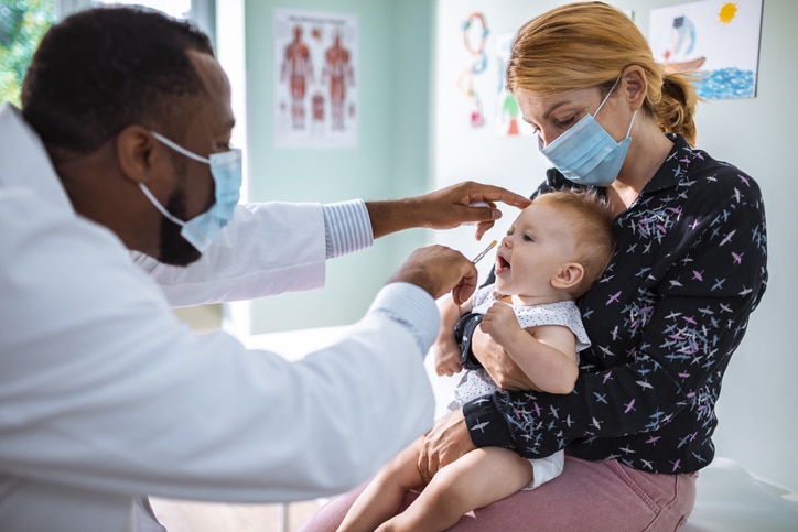 A physician administering care and medication to a baby in a parent's arms