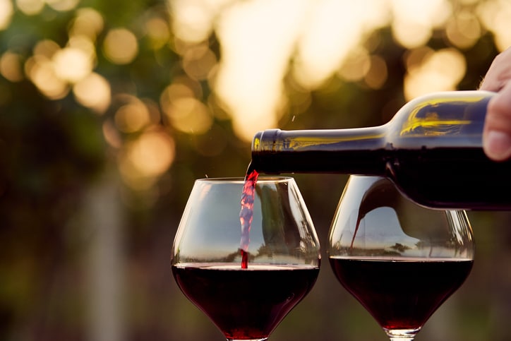 Red wine in a bottle being poured into glasses